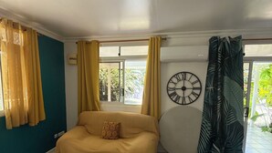 Una habitación con un sofá, una mesa de centro de madera, un reloj de pared y una ventana con cortinas.