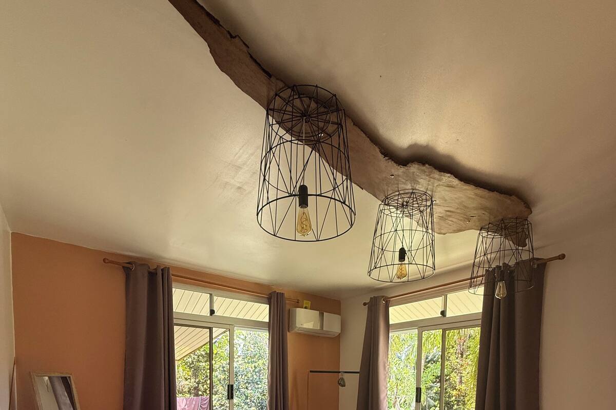 A bedroom with a bed, a wooden dresser, a round table, and two windows with curtains.