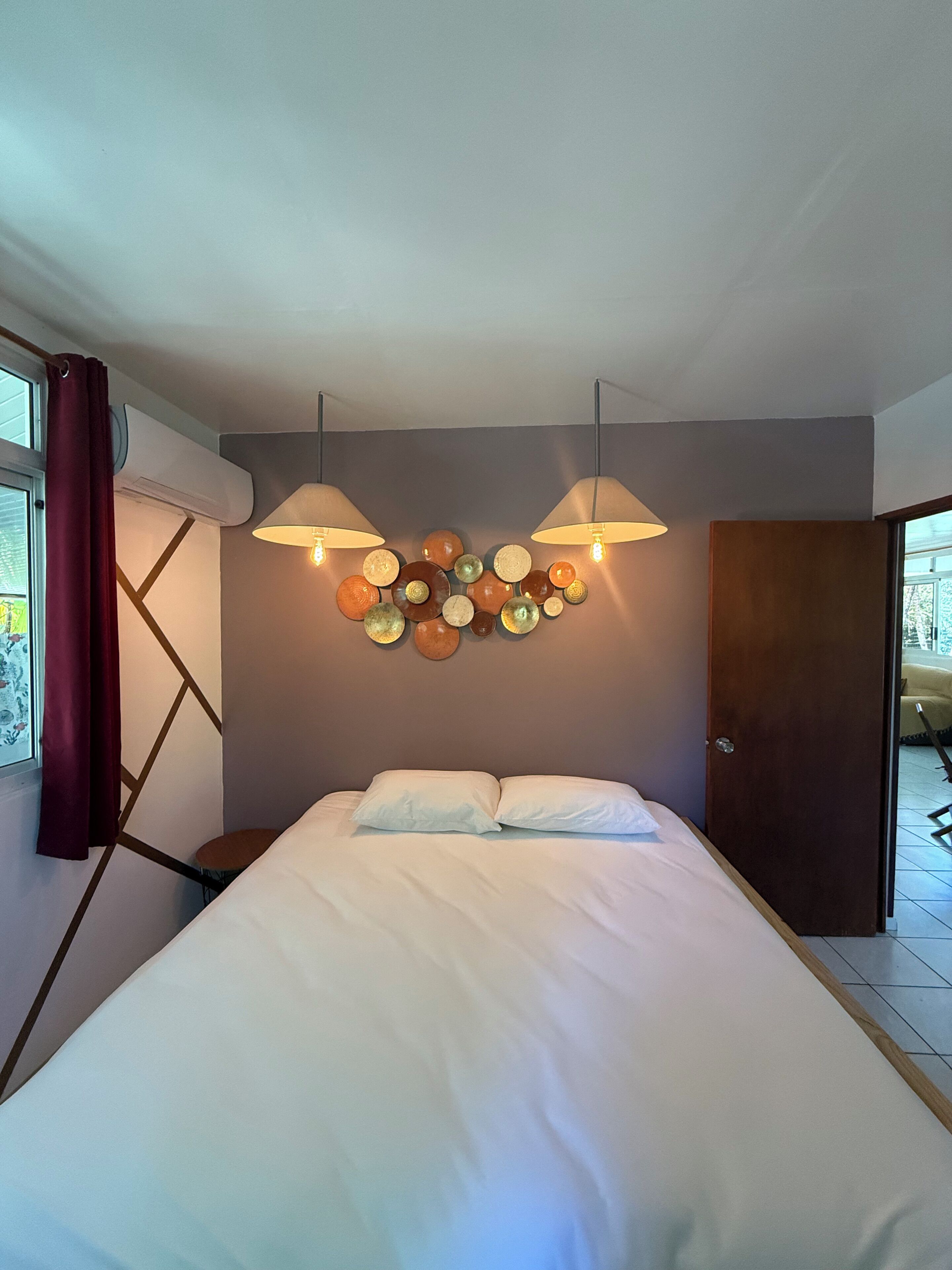 A bedroom with a bed, two wall-mounted lamps, a decorative wall piece, and a door.
