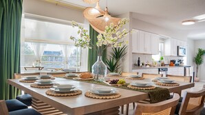 A modern kitchen with a large island, white cabinets, and a dining area with a green table runner. - The Don | Fully Loaded Waterfront Wellness (Tampa)