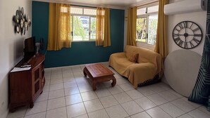A living room with a sofa, a coffee table, a TV stand, and a wall clock. - Vahine Ori Lodge (Tumaraa)