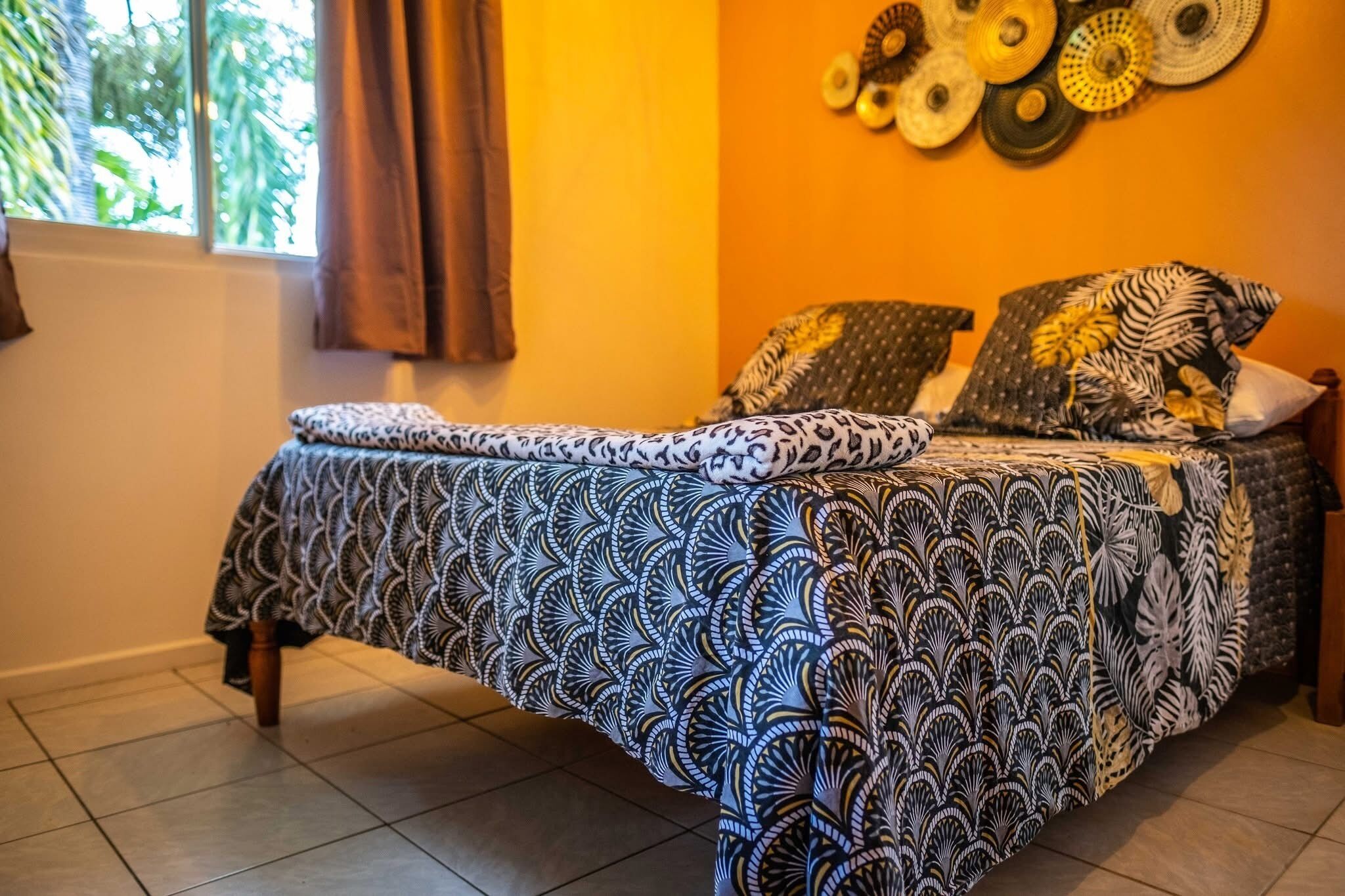 A bedroom with a bed covered in a patterned bedspread, a window with curtains, and a wall decorated with circular wall art.