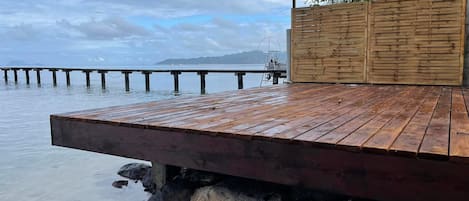 A wooden deck extending over water, with a view of a distant island and a wooden fence.