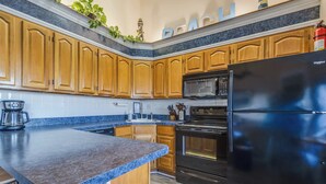 Una cucina con mobili in legno, un frigorifero nero, un forno a microonde e una macchina da caffè.