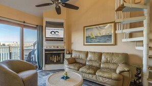 Un soggiorno con un divano in pelle, un tavolino da caffè rotondo in vimini, un quadro incorniciato con barche a vela e un cartello per Ocean City Vacation Homes.