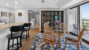 A modern kitchen with a stainless steel refrigerator, a dining area with a glass table and wicker chairs, and a ceiling fan. - 9400 Building #401 (Ocean City)