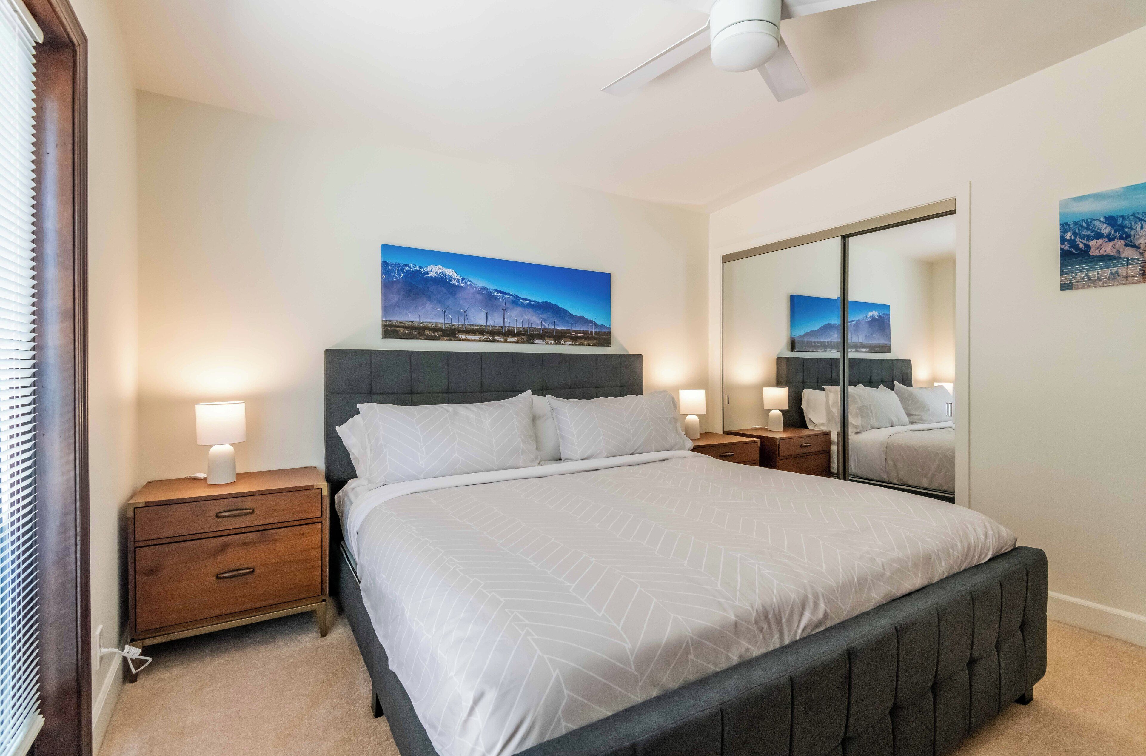 A bedroom with a bed, nightstands, a mirror, and wall art.