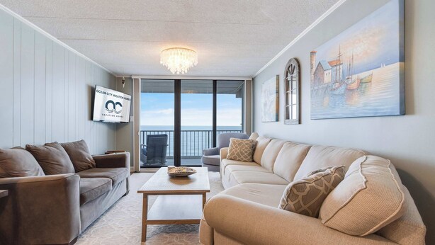 A spacious living room with a large window, a chandelier, and a painting of a harbor scene. - Sea Terrace 801 (Ocean City)
