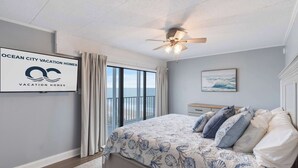 A bedroom with a bed, a ceiling fan, a window with curtains, a framed picture, and a sign on the wall. - Sea Terrace 801 (Ocean City)