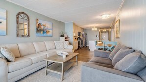 A living room with a beige sofa, a grey sofa, and a wooden coffee table. There is a kitchen in the background with a refrigerator, stove, and cabinets. - Sea Terrace 801 (Ocean City)