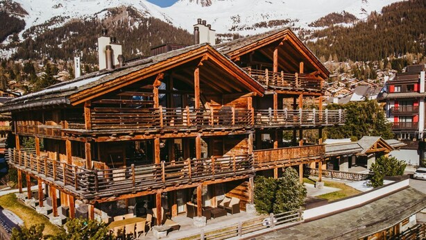 Eine Holzchalet mit mehreren Balkonen und Blick auf schneebedeckte Berge.