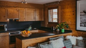 Eine moderne Küche mit Holzschränken, einer zentralen Kochinsel mit Obstschale und einer gemütlichen Sitzecke mit Sofa und Kissen.