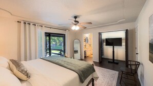 Ein Schlafzimmer mit Bett, Deckenventilator, Fernseher und Blick ins Freie.