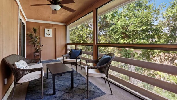 A balcony with wicker furniture, a ceiling fan, and a view of trees.