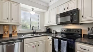 A modern kitchen with white cabinetry, a black microwave, and a stainless steel dishwasher.