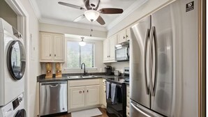 A modern kitchen with stainless steel appliances, white cabinetry, and a ceiling fan.
