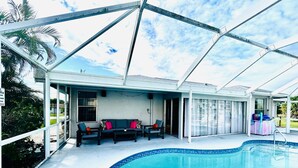 A covered outdoor swimming pool with a patio area, including seating and a covered entryway. - Pink Pineapple ~ Walk to Downtown ~ Chic Heated Pool Home (Cape Coral)