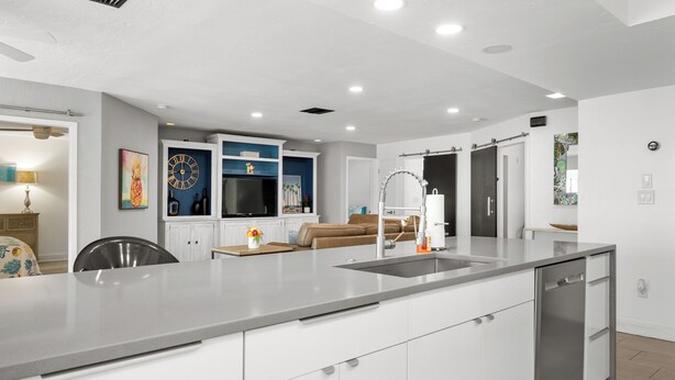 A modern kitchen with white cabinets, a stainless steel dishwasher, and a built-in oven. - Pink Pineapple ~ Walk to Downtown ~ Chic Heated Pool Home (Cape Coral)