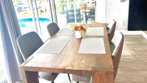 A wooden conference table with two placemats, a vase with flowers, and six chairs. - Pink Pineapple ~ Walk to Downtown ~ Chic Heated Pool Home (Cape Coral)