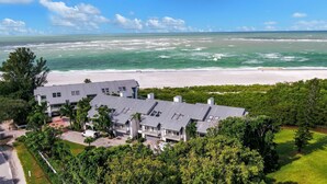 Une grande maison moderne, dotée d’un toit plat et de nombreux balcons, entourée d’une végétation luxuriante et donnant sur une plage.
