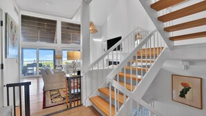 Un vaste espace de vie avec une grande fenêtre donnant sur un balcon, un escalier à marches en bois et un aménagement intérieur moderne.