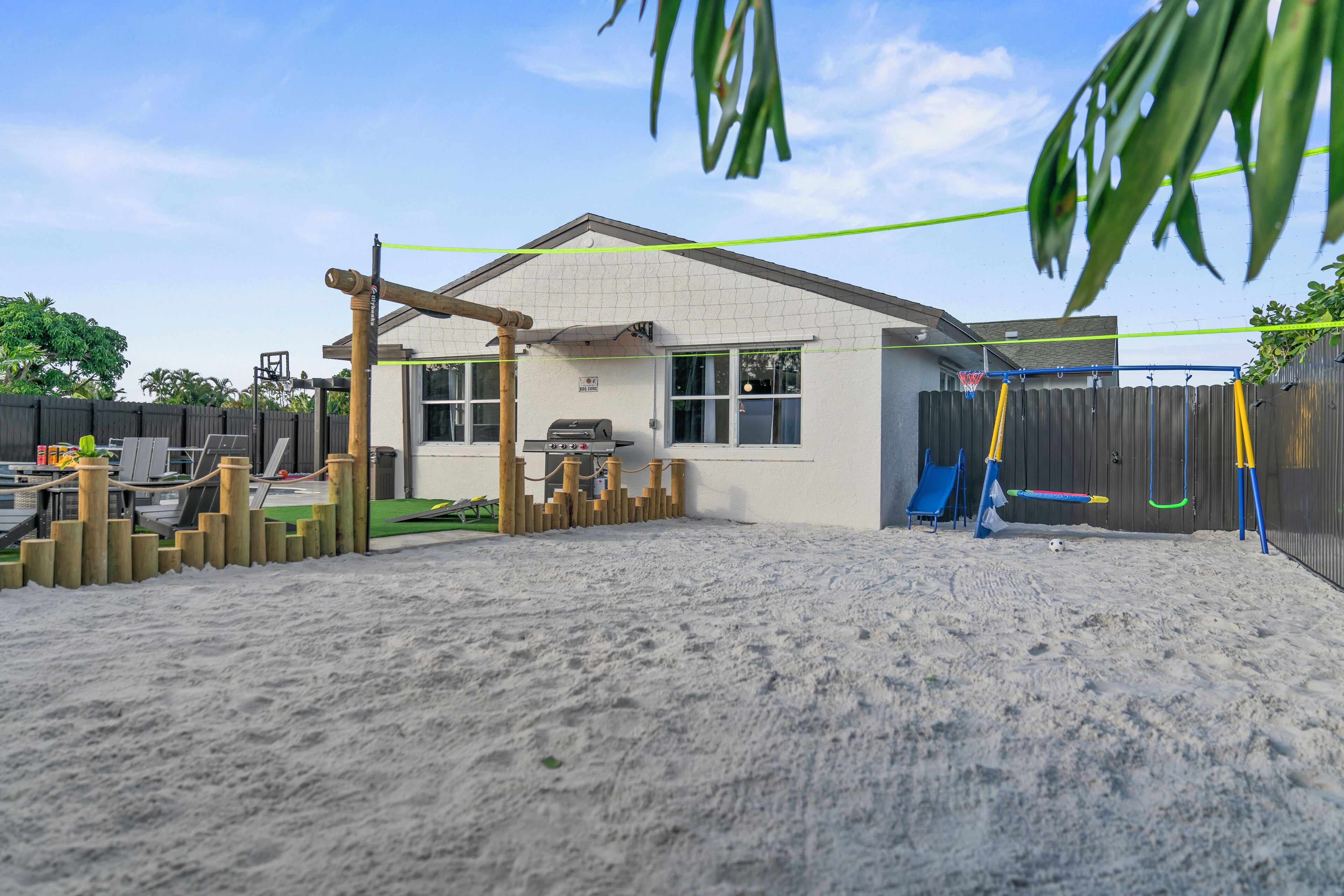 Uma casa com quintal de areia, um parquinho de madeira e um escorregador azul.