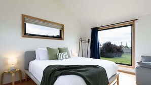 Un dormitorio con cama, mesita de noche, ventana y vistas al exterior.