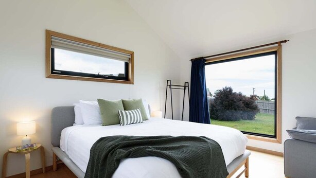 Een slaapkamer met een bed, nachtkastje, raam en uitzicht op het omliggende landschap.