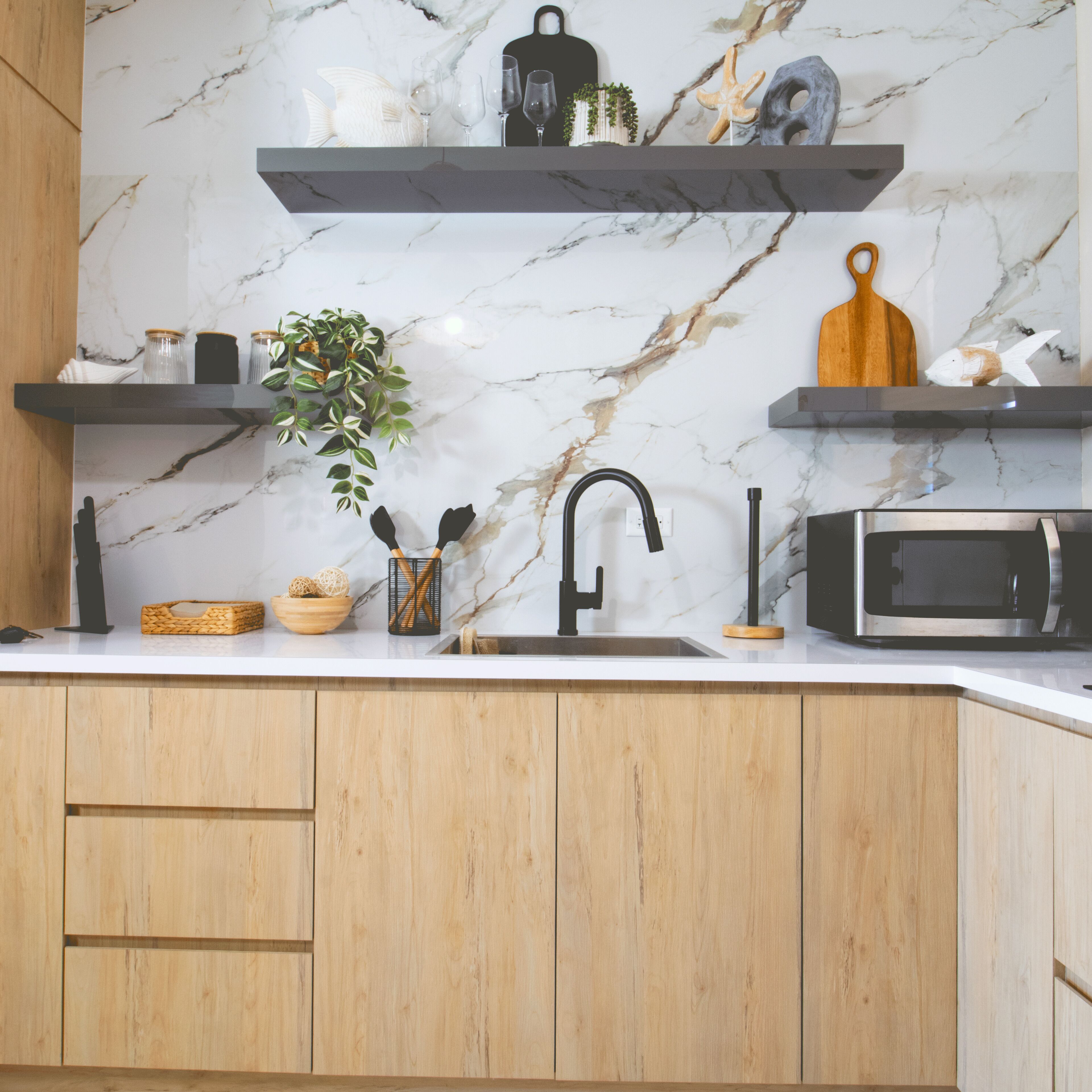 A kitchen with marble backsplash, wooden cabinets, a sink, a microwave, and various kitchen utensils and decorations.