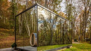 Eine moderne Glasarchitektur mit einem hölzernen Fass im Zentrum, umgeben von einem Wald.