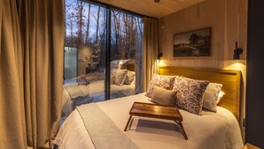 Ein Schlafzimmer mit einem großen Bett, einem Holzkopfteil, einem Nachttisch und Blick durch eine Glastür.