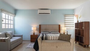 Une chambre à coucher comprenant un lit, deux tables de chevet, une commode, un canapé, un meuble en bois et une fenêtre avec des stores.