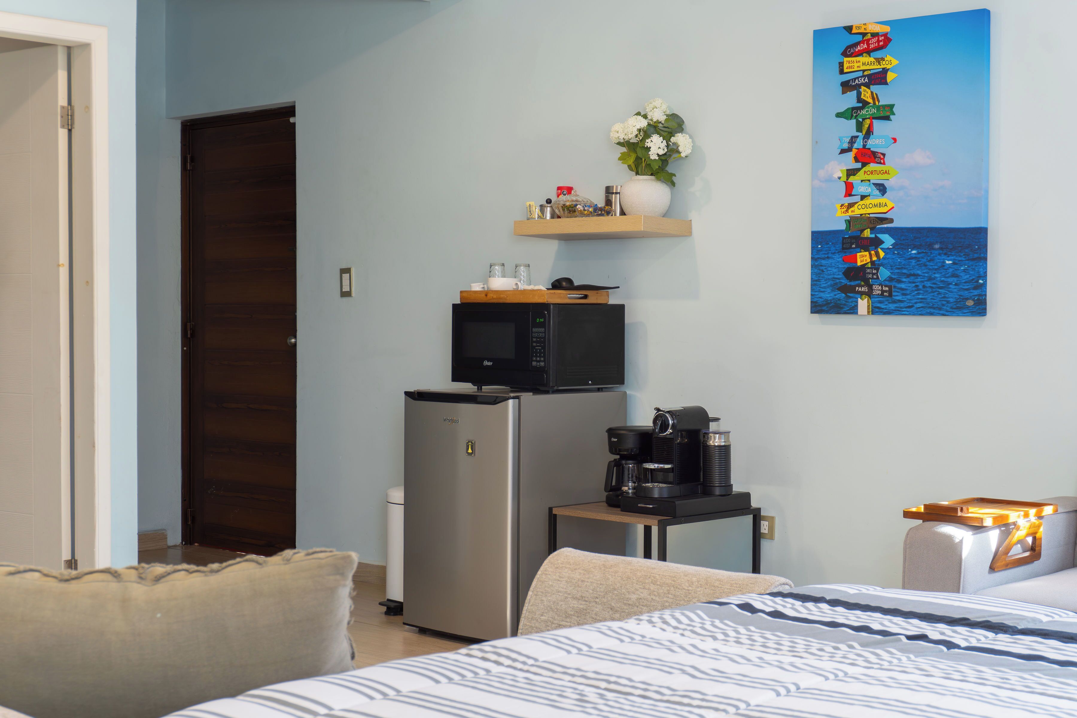 Ein Hotelzimmer mit einem Bett, einer kleinen Küchenzeile inklusive Mikrowelle, einer Kaffeemaschine und einem Regal mit Blumenvas und einem Schild.