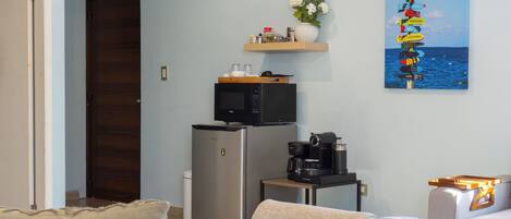 Ein Hotelzimmer mit einem Bett, einer kleinen Küchenzeile inklusive Mikrowelle, einer Kaffeemaschine und einem Regal mit Blumenvas und einem Schild.