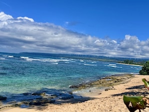 A beach with clear water, a sandy shore, and distant wind turbines. - Beachy Bungalow (Waialua)