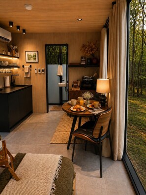 A modern kitchen with a built-in oven, a dining area with a round table, and a view of the outdoors through large windows.