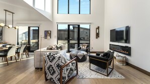 Un salón amplio con techo alto, ventanas grandes, chimenea y televisor de pantalla plana.