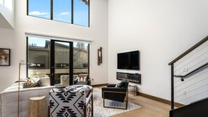 Amplia sala de estar con techos altos, chimenea, televisor grande y escalera.