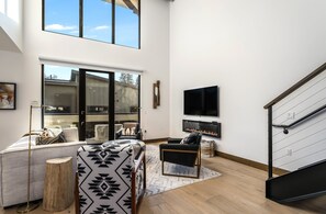 Ein geräumiges Wohnzimmer mit hoher Decke, Kamin, großem Fernseher und einer Treppe.