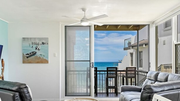 A balcony with a view of the sea, a ceiling fan, and a painting of boats. - Oceanfront Stay Steps to the Sand (The Entrance)