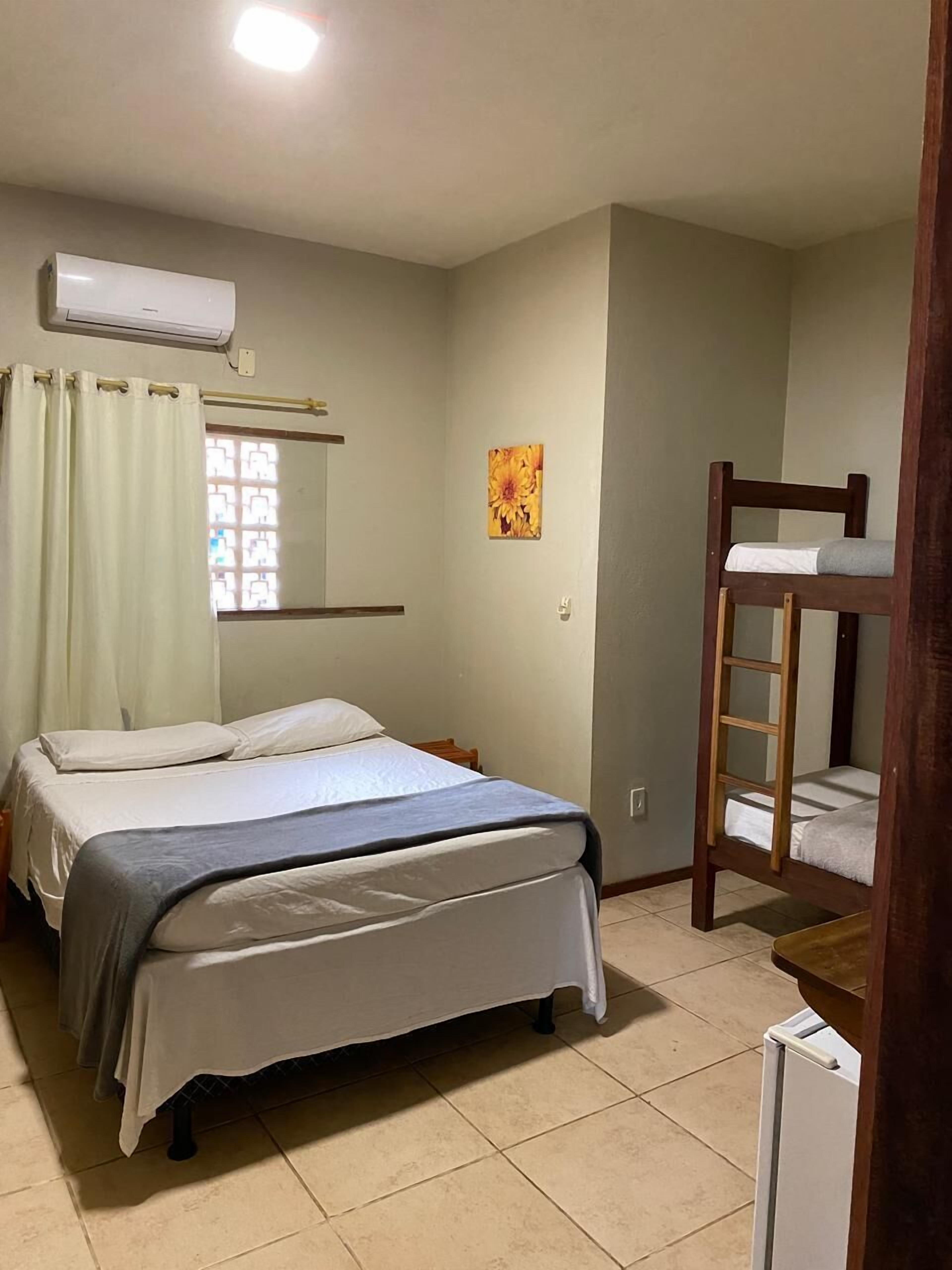 Un dormitorio con cama, literas, una ventana con cortinas, aire acondicionado y un cuadro pequeño en la pared.