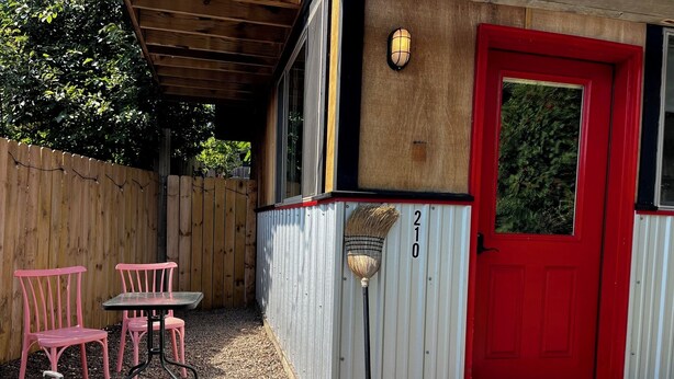 A covered patio area with a red door, numbered 210, and a small table with chairs.