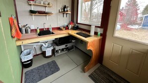 A compact kitchen with a wooden countertop, built-in shelves, a window, and a door.