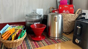 A kitchen counter with a coffee maker, a kettle, a basket of snacks, and a box of coffee.