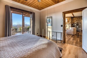 A bedroom with a large bed, a view of the outdoors, and a stone wall in the background. - Luxury Lodge: Heated Pool, Spa, Mountain Views, Sleeps 16 (blue ridge)