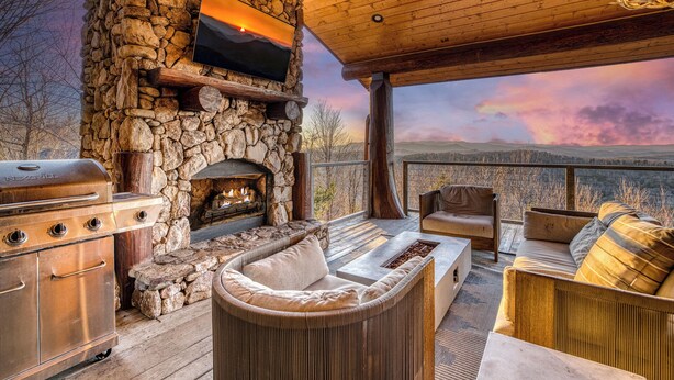 Ein Kamin aus Stein mit einem Fernseher darüber, ein Grill und Sitzgelegenheiten im Freien mit Blick auf die Berge.