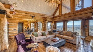 Ein Holzblockhaus-Interieur mit einem großen Wohnbereich, einem Esstisch und Blick auf die Berge.