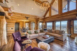 A log cabin interior with a large living area, a dining table, and a view of the mountains. - Luxury Lodge: Heated Pool, Spa, Mountain Views, Sleeps 16 (blue ridge)