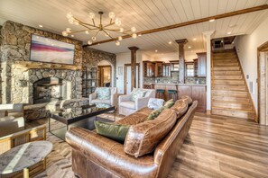 A spacious living area with a stone fireplace, leather sofa, and a modern chandelier. - Luxury Lodge: Heated Pool, Spa, Mountain Views, Sleeps 16 (blue ridge)