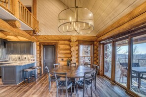 A log cabin interior with a wooden dining table, chairs, a kitchen area, and large windows. - Luxury Lodge: Heated Pool, Spa, Mountain Views, Sleeps 16 (blue ridge)